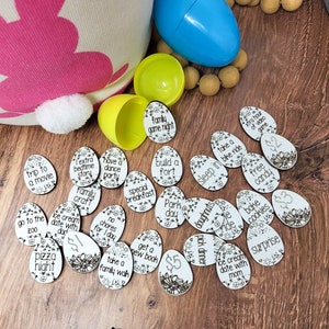May include: A set of 16 white wooden Easter eggs with black floral designs and text. Each egg has a different activity or treat written on it, such as "trip to a movie", "ice cream date with dad", "free candy", and "build a fort".