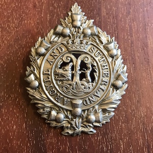 May include: A silver metal badge with a thistle design and the words "The Highland and Sutherland Regiment" around the edge.