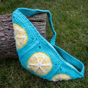 May include: A crocheted turquoise bag with a long strap. The bag is decorated with yellow and white crocheted lemon slices.