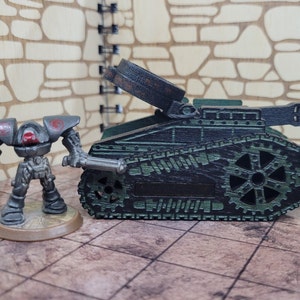 May include: A dark green toy tank with a black and silver cannon. The tank has a detailed design with gears and tracks. A small, gray robot stands next to the tank.