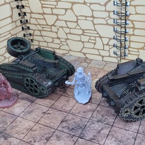 May include: Two miniature, green and black, tracked vehicles with large wheels. A miniature, gray, skeletal figure with a hat and a weapon stands between the vehicles.