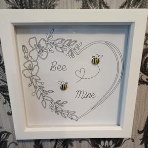 May include: A white framed picture with a black and white drawing of a heart with flowers and bees. The text "Bee Mine" is written inside the heart.