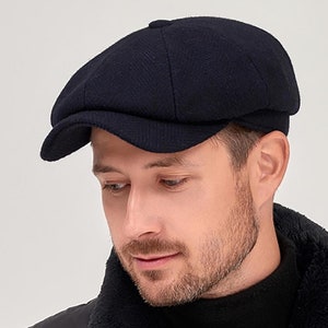 Puede incluir: Una gorra de newsboy de lana azul marino con una visera ligeramente curvada. La gorra está hecha de un tejido suave y texturizado y tiene un diseño clásico y atemporal.