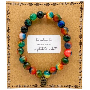 May include: A handmade flower agate crystal bracelet with colorful beads in shades of red, orange, yellow, green, blue, and black. The bracelet is displayed on a brown card with decorative diamond shapes and the words "handmade - flower agate - crystal bracelet".