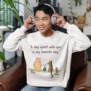 May include: A white sweatshirt with a Winnie the Pooh and friends graphic. The text on the sweatshirt reads "A day spent with you is my favorite day."