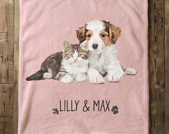 Może przedstawiać: Różowy koc z polaru z nadrukiem brązowego i białego psa oraz brązowego i białego kota. Pod zwierzętami nadrukowany jest tekst "Lilly & Max".