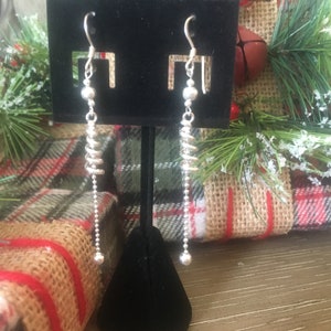 May include: A pair of silver dangle earrings with a spiral design and a small bead at the bottom.