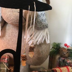 May include: A pair of silver dangle earrings with a small, clear, iridescent stone and a larger, orange, faceted stone at the bottom of each earring.