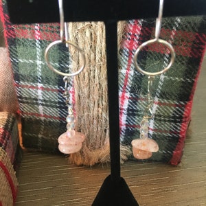 May include: A pair of silver earrings with a small, round, peach-colored stone and clear beads hanging from a silver hoop.