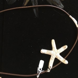 May include: A silver starfish pendant on a brown leather cord necklace.
