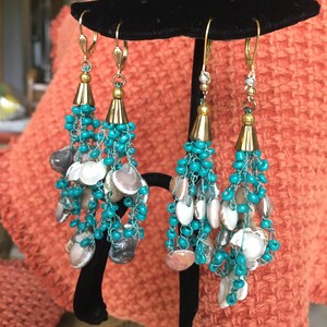 May include: A pair of turquoise and gold dangle earrings with a cluster of small seashells. The earrings are made with tiny beads and have a tassel-like design.
