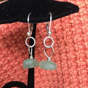 May include: A pair of silver dangle earrings with light green glass beads. The earrings have a simple design with a small circle at the top and a larger, rounded bead at the bottom.