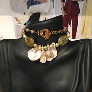 May include: A multi-strand necklace with brown, green, and gold beads, and a large, pink, shell pendant.