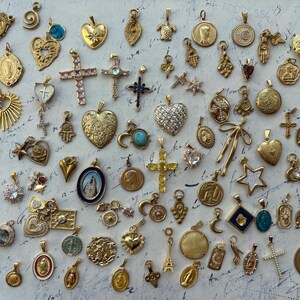 Puede incluir: Una colecci&oacute;n de dijes dorados con varios dise&ntilde;os religiosos, de la naturaleza y abstractos. Los dijes est&aacute;n dispuestos sobre una superficie de color claro.