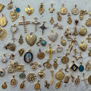 Puede incluir: Una colecci&oacute;n de dijes dorados con varios dise&ntilde;os religiosos y simb&oacute;licos, incluyendo corazones, cruces, estrellas y llaves. Los dijes est&aacute;n dispuestos sobre un fondo blanco.