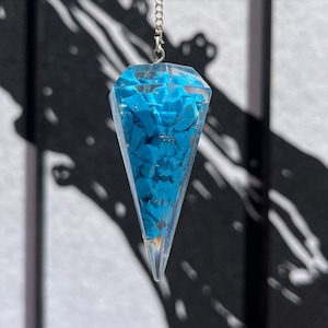 May include: A blue crystal pendulum with a silver chain. The crystal is a clear, faceted shape filled with small blue pieces.