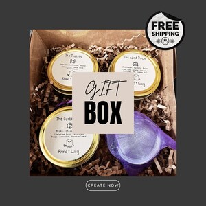 May include: A gift box filled with three small jars of candles, each with a different scent and label. The labels include "The Digestif", "The Wind Down", and "The Curto". The box is filled with brown crinkled paper and a purple mesh bag.