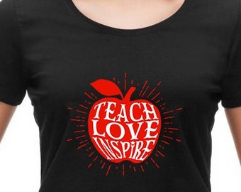May include: Black t-shirt featuring a red apple graphic. The apple has the words "Teach Love Inspire" written inside it.