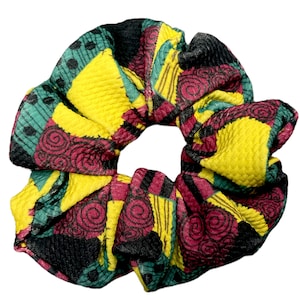 May include: A colorful scrunchie with a patchwork design. The fabric features squares of yellow, black, teal, and burgundy, with spiral and dotted patterns. This hair accessory adds a pop of color and style.