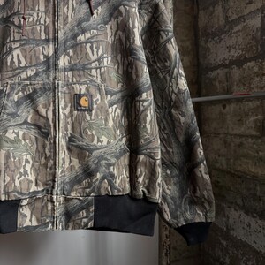 Puede incluir: Chaqueta Carhartt con cremallera y estampado de camuflaje en tonos marrones, verdes y grises. La chaqueta tiene un dobladillo y pu&ntilde;os de canal&eacute; negros, un bolsillo delantero y el parche con el logotipo de Carhartt.