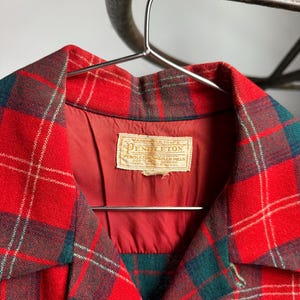 K&ouml;nnte beinhalten: Eine rot, gr&uuml;n und wei&szlig; karierte Jacke mit Kragen. Die Jacke h&auml;ngt an einem Metallb&uuml;gel. Das Etikett in der Jacke lautet "Pendleton" und enth&auml;lt Text.