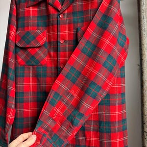 K&ouml;nnte beinhalten: Ein rot, gr&uuml;n und braun kariertes Hemd mit Kn&ouml;pfen. Das lang&auml;rmlige Hemd hat zwei Vordertaschen und einen Kragen. Das Karomuster ist ein klassisches Design, mit Rot als Hauptfarbe und gr&uuml;nen und braunen Akzenten.