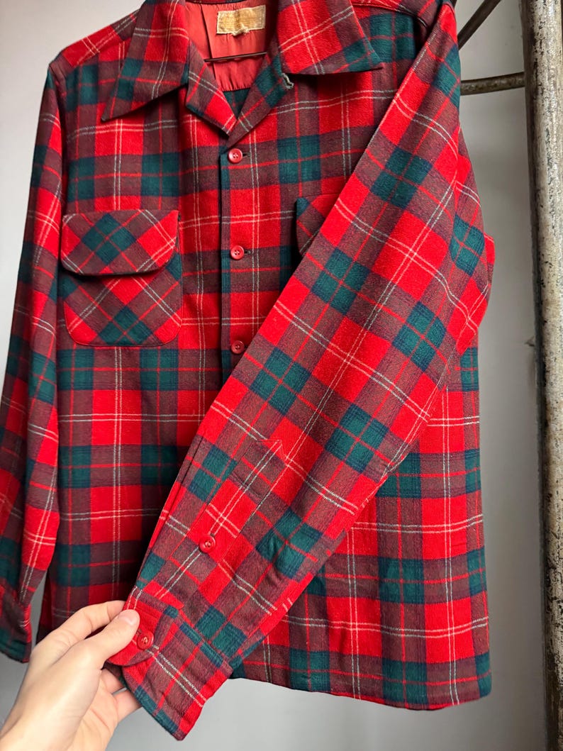 K&ouml;nnte beinhalten: Ein rot, gr&uuml;n und braun kariertes Hemd mit Kn&ouml;pfen. Das lang&auml;rmlige Hemd hat zwei Vordertaschen und einen Kragen. Das Karomuster ist ein klassisches Design, mit Rot als Hauptfarbe und gr&uuml;nen und braunen Akzenten.