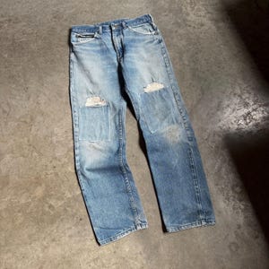 May include: Light blue denim jeans with distressed patches on the knees and thighs. The jeans have a classic five-pocket design and a faded wash, giving them a vintage look. The patches are a lighter shade of blue.