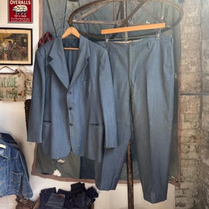 May include: A blue suit consisting of a single-breasted blazer with three buttons and matching trousers. The blazer features notched lapels, long sleeves, and two front pockets. The trousers have a straight-leg cut and a clean, pressed finish.