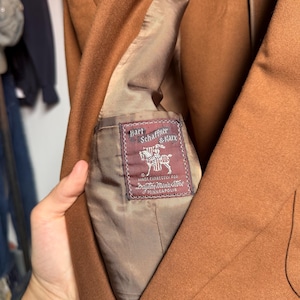 May include: A tan blazer with a brown interior lining featuring a rectangular label that reads Hart Schaffner & Marx, Made Expressly For Dayton Men's Store Minneapolis, accompanied by a graphic illustration of a knight on a horse.