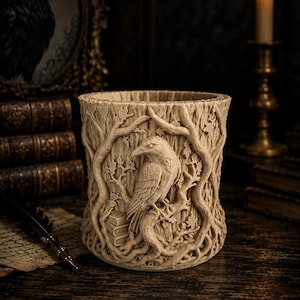 May include: A cylindrical beige vessel featuring a detailed relief carving of a raven perched on a branch amidst intertwined tree roots and leaves. The exterior surface displays a textured, wood-like appearance with a stack of books near the raven.