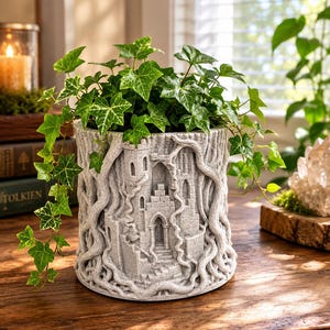 May include: A cylindrical gray stone planter featuring a relief sculpture of a castle surrounded by winding vines. The planter contains a lush green ivy plant with variegated leaves that spill over the textured, castle-adorned exterior walls.
