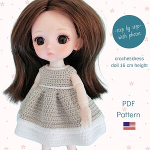 May include: A doll with brown hair wearing a crocheted dress. The dress is beige with a white trim. The doll is 16 cm tall. Text on the image says "-step by step- with photos", "crochet dress", and "PDF Pattern".