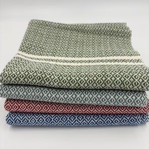 May include: A stack of four folded woven cotton towels in shades of green, gray, red, and blue. Each towel features a diamond pattern. The top green towel has a white stripe across the middle.