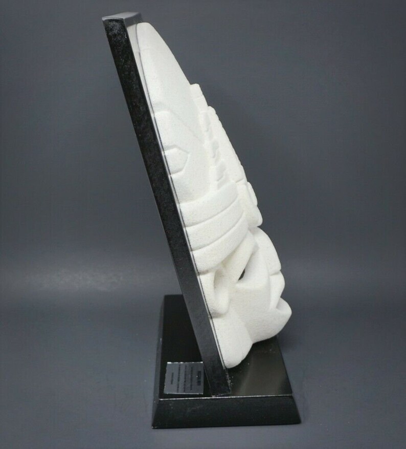 Peut inclure: Masque en pierre blanche sculpt&eacute;e avec des d&eacute;tails complexes, mont&eacute; sur un socle en bois noir.