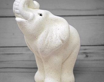 May include: White ceramic elephant figurine with a textured, sparkly finish. The elephant is standing with its trunk raised in the air.
