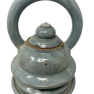 May include: A blue ceramic teapot with a unique handle and a layered design. The teapot has a speckled glaze and a rounded lid.