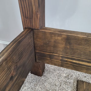 May include: Close-up of a wooden bed frame corner, showing the dark brown stained wood and the way the pieces are joined together.
