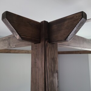 May include: Close-up of the top corner of a wooden bed frame. The frame is made of dark brown wood with a natural wood grain. The corner is joined with a simple, angled design.