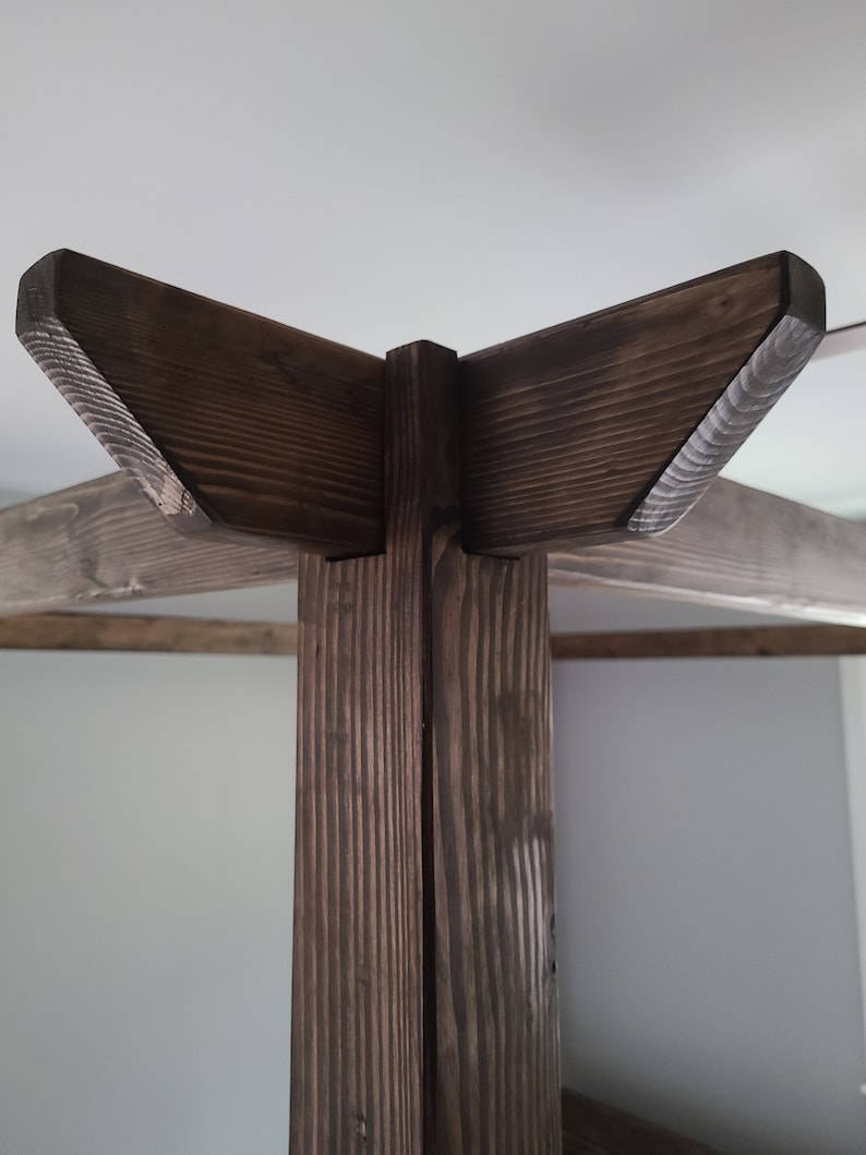 May include: Close-up of the top corner of a wooden bed frame. The frame is made of dark brown wood with a natural wood grain. The corner is joined with a simple, angled design.