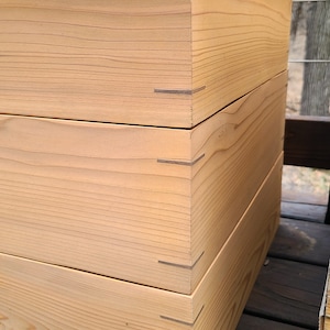 May include: A wooden box with a natural finish. The box is made of three stacked pieces of wood, each with a visible grain pattern. The box is sitting on a wooden surface.