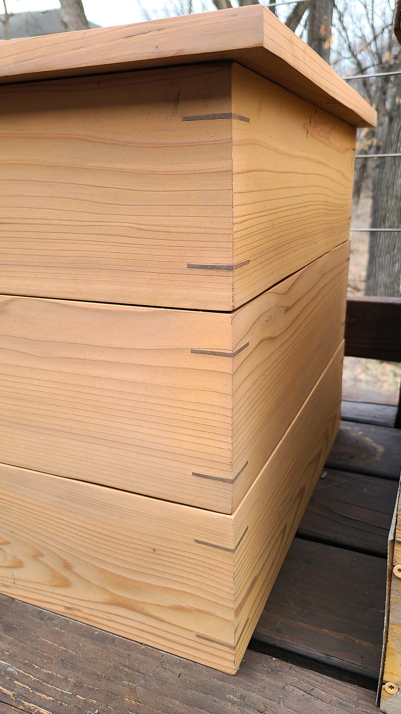May include: A wooden box with a natural finish. The box is made of three stacked pieces of wood, each with a visible grain pattern. The box is sitting on a wooden surface.