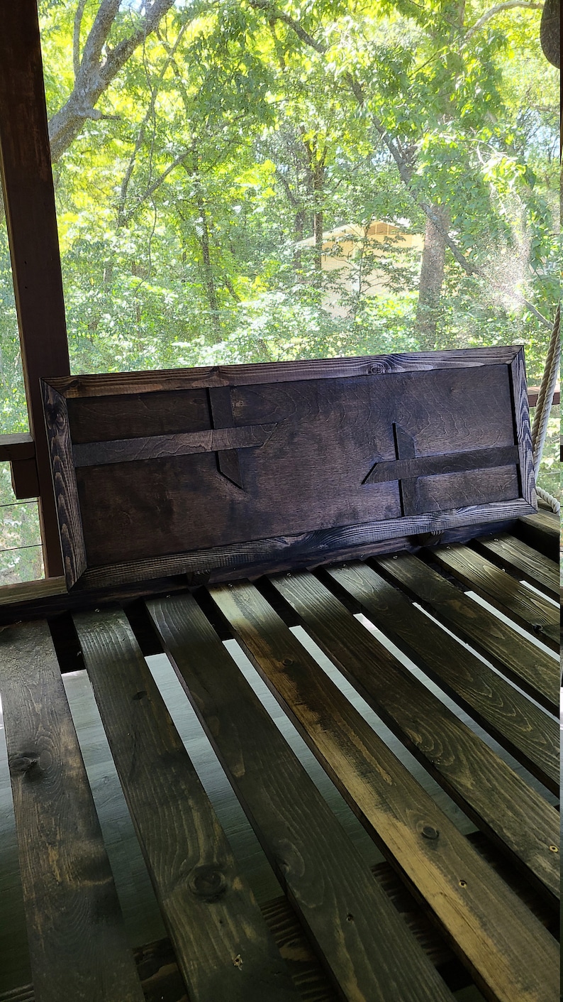 May include: A dark brown wooden sign with a carved Texas-shaped design. The sign is hanging on a wooden porch swing.