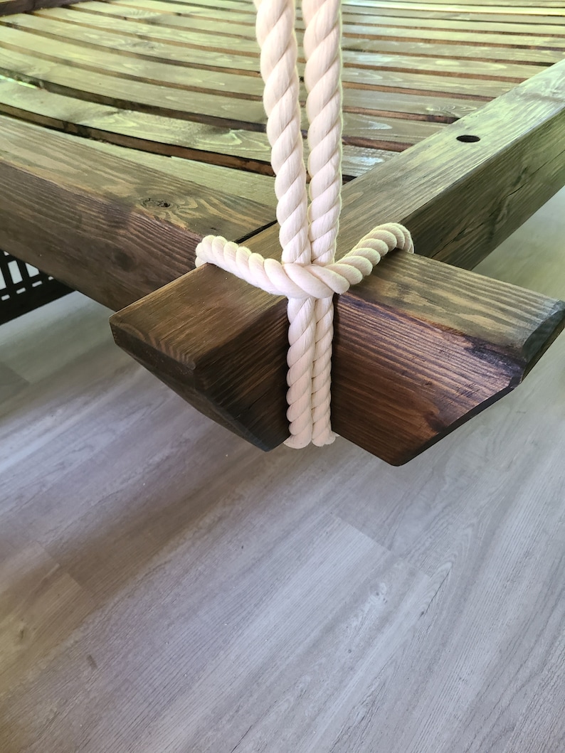 May include: Close-up of a wooden swing frame with a white rope attached. The rope is tied in a knot and the frame is stained a dark brown color.