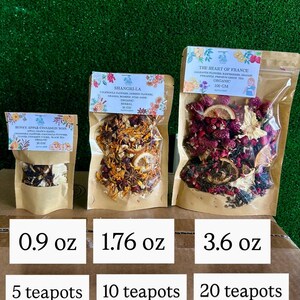 May include: Three sealed bags of organic herbal tea blends. The bags are labeled with the names "Honey Apple Cinnamon Noir", "Shangri-La", and "The Heart of France". Each bag contains a different blend of dried flowers, fruits, and herbs. The bags are labeled with the weight in ounces and the number of teapots.