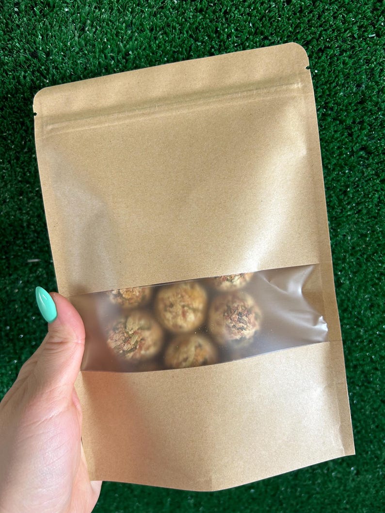 May include: A brown paper bag with a clear plastic window, showing a variety of round, brown, and beige treats inside.