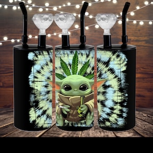 Op de afbeelding: Drie zwarte en groene glazen waterpijpen met een tie-dye patroon en een cartoon afbeelding van een groen wezen dat een bong en een joint vasthoudt.