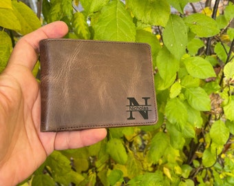 May include: A brown leather wallet with a personalized initial "N" and the name "Nicholas" engraved on the front.