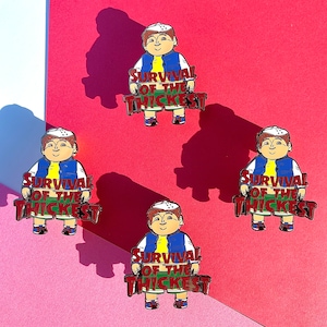 K&ouml;nnte beinhalten: Vier Emaille-Pins mit einer Comicfigur, die eine blaue Jacke und eine wei&szlig;e M&uuml;tze tr&auml;gt. Jeder Pin tr&auml;gt die Aufschrift "Survival of the Thickest" in roten Buchstaben.