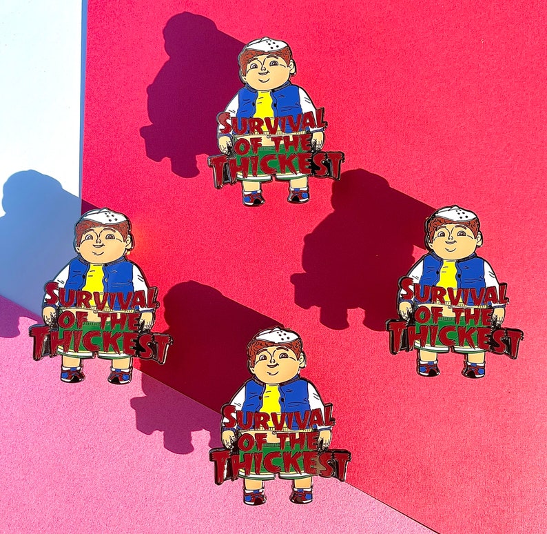 K&ouml;nnte beinhalten: Vier Emaille-Pins mit einer Comicfigur, die eine blaue Jacke und eine wei&szlig;e M&uuml;tze tr&auml;gt. Jeder Pin tr&auml;gt die Aufschrift "Survival of the Thickest" in roten Buchstaben.